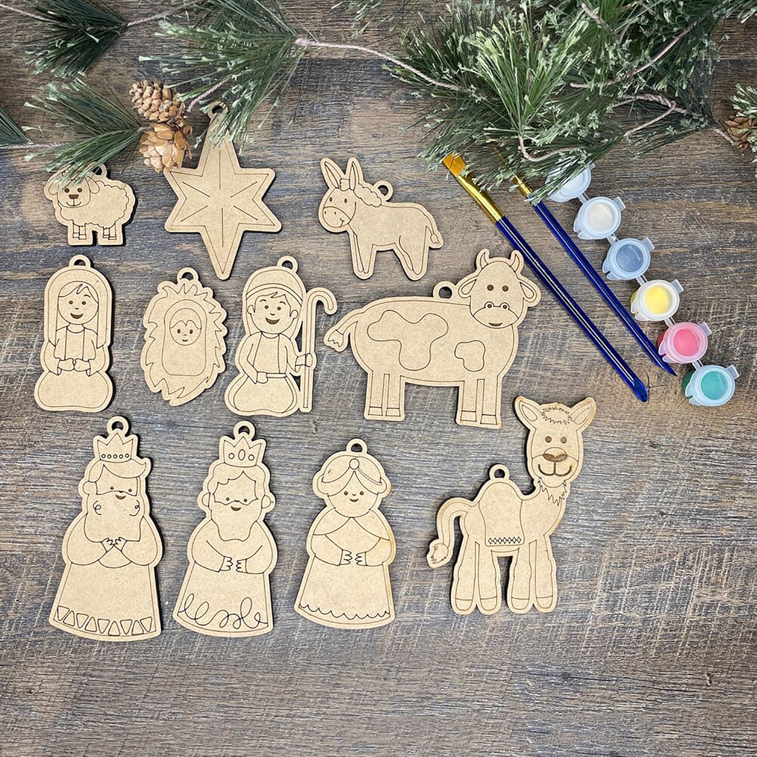 Set of wooden nativity scene ornaments with paintbrushes and paint on a wooden surface.