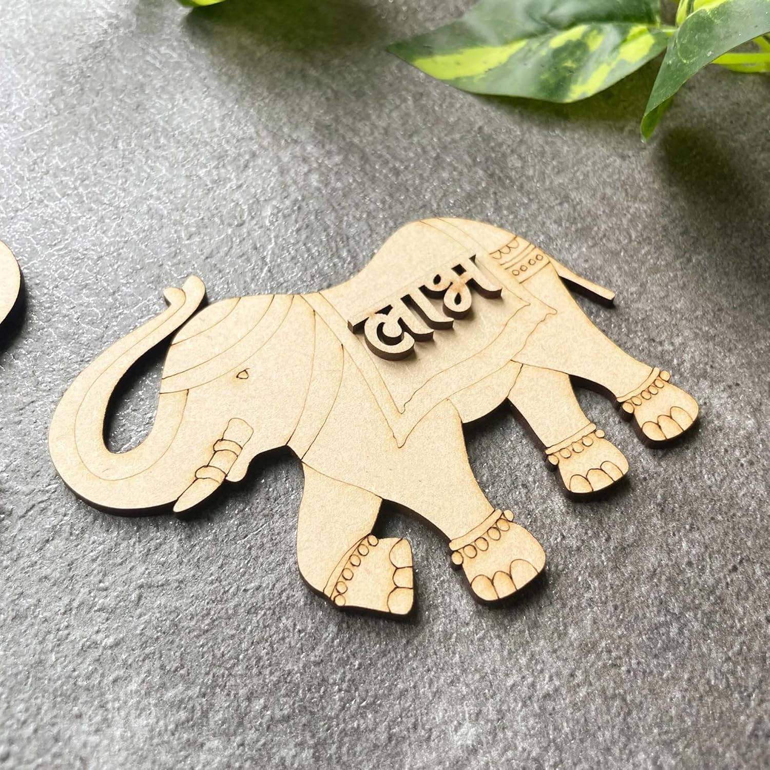 Wooden elephant ornament with engraved text on a gray surface with green leaves.