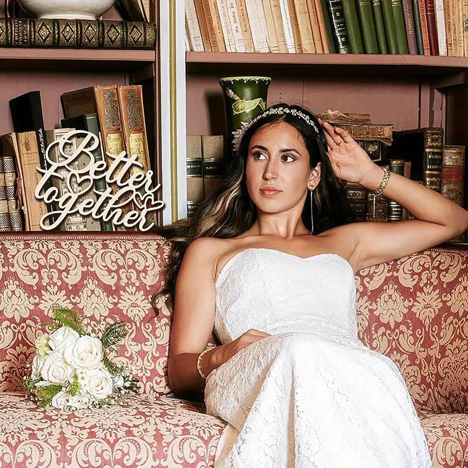 Woman in a white dress sitting on a patterned couch with a 'Better Together' sign and books in the background.