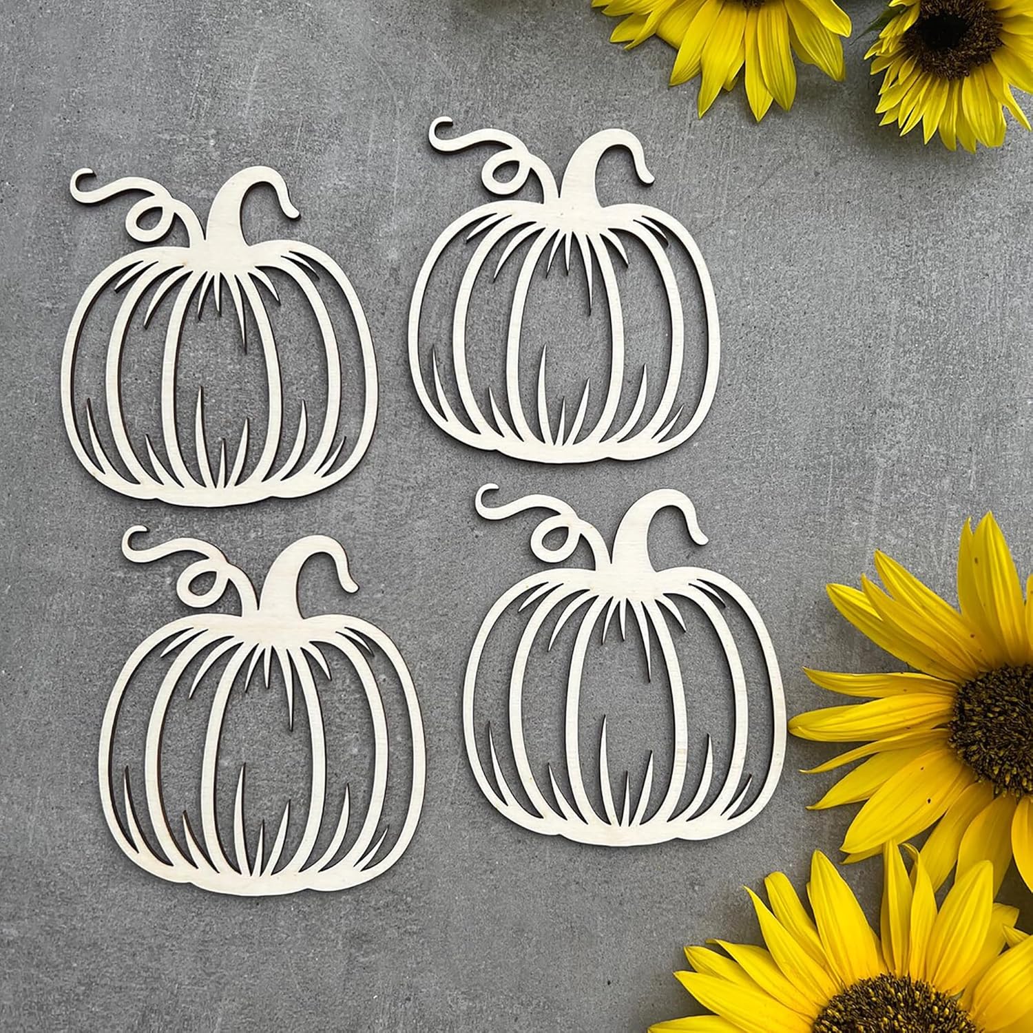 Four white pumpkin-shaped cutouts on a gray surface with yellow sunflowers.