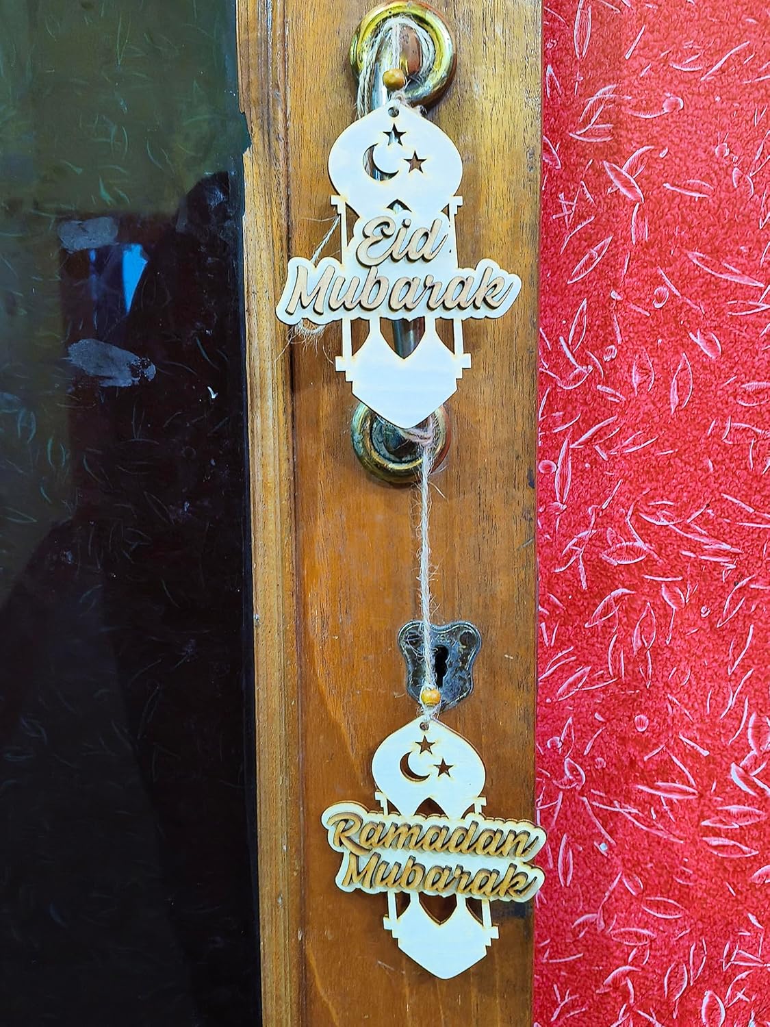 Decorative hanging with 'Eid Mubarak' and 'Ramadan Mubarak' text on a wooden and red fabric background.