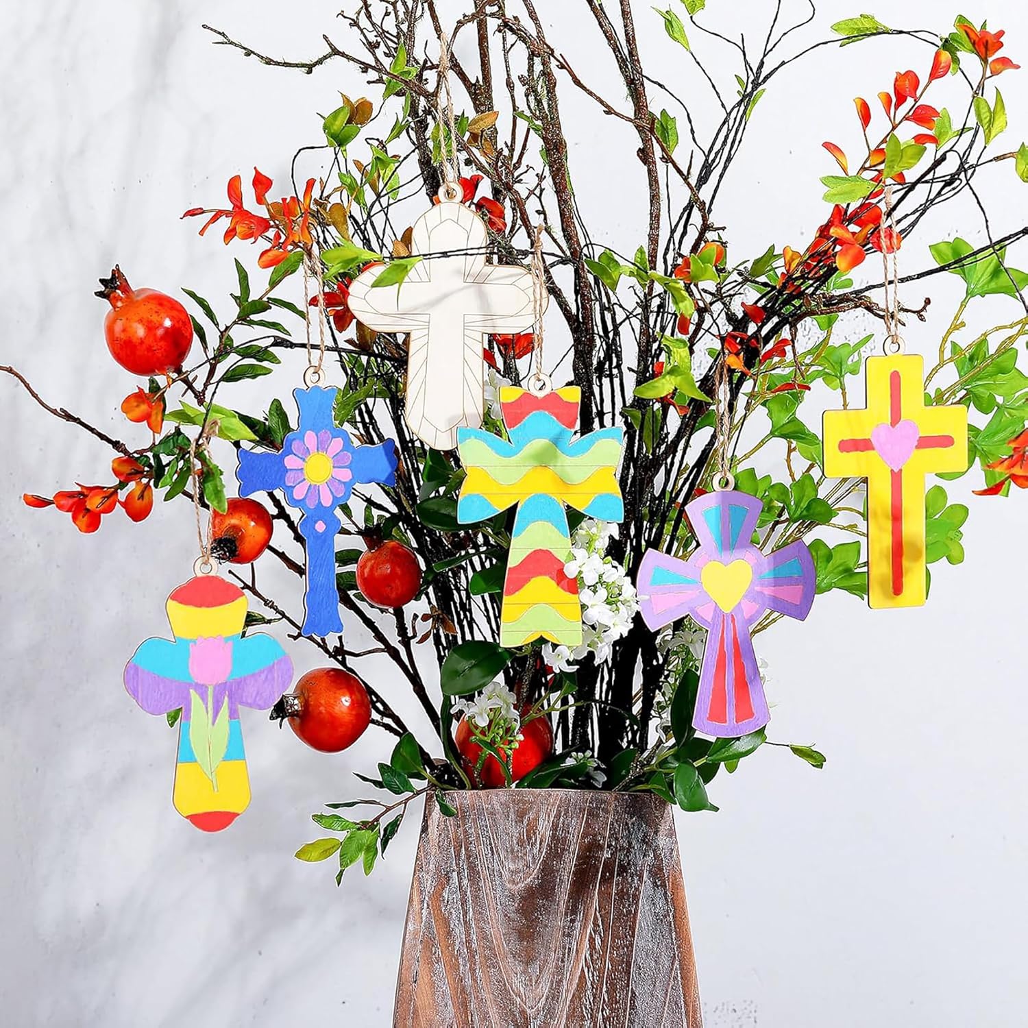 Decorative cross ornaments hanging from a branch with flowers and fruits.