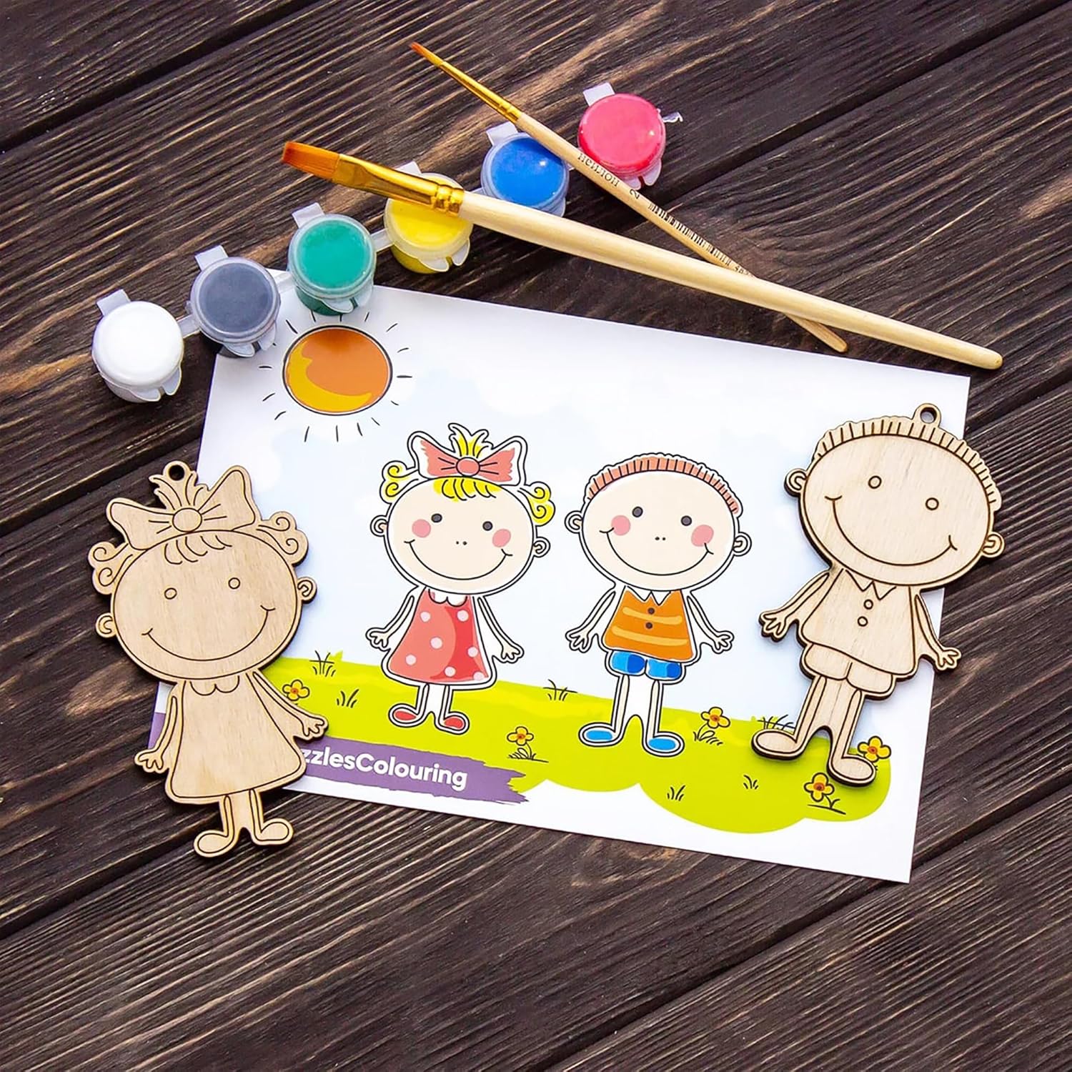 Wooden cutouts of children and a sun with paint and brushes on a coloring sheet.