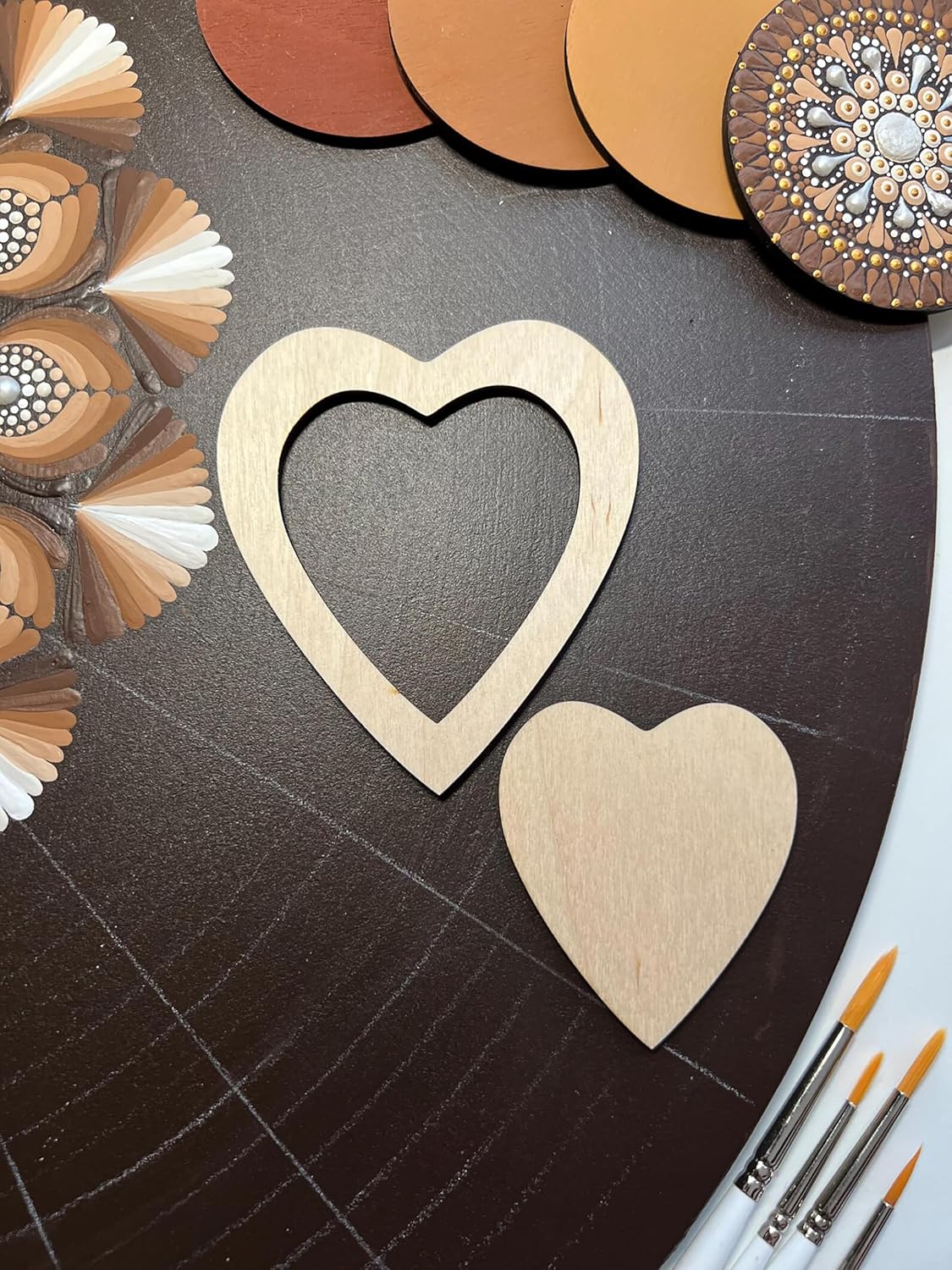 Wooden heart shapes on a dark surface with paintbrushes and color swatches.