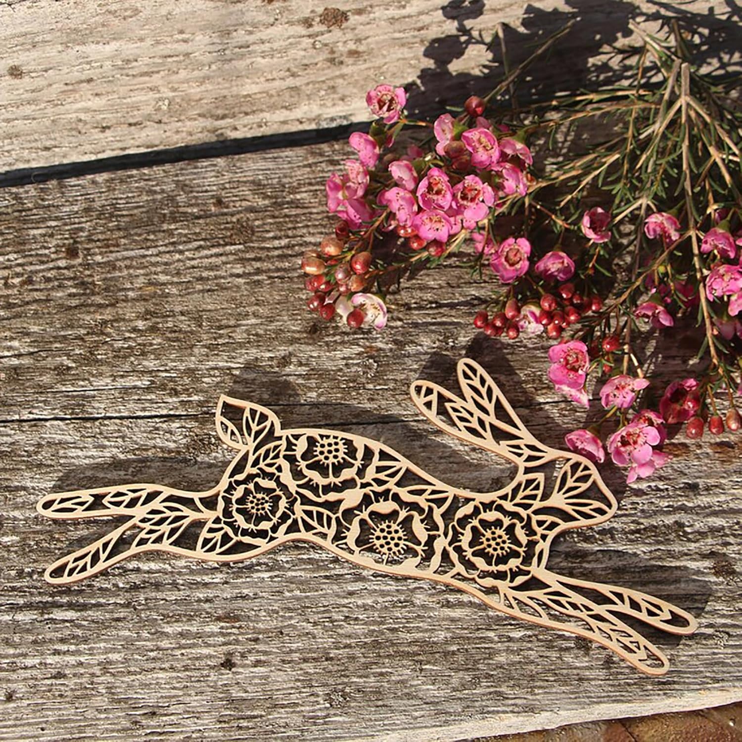 Decorative hare-shaped object with floral patterns on a wooden surface with pink flowers.
