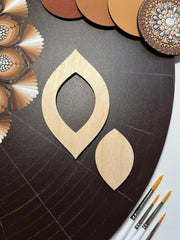 Wooden earring shapes on a dark surface with paintbrushes and color swatches.