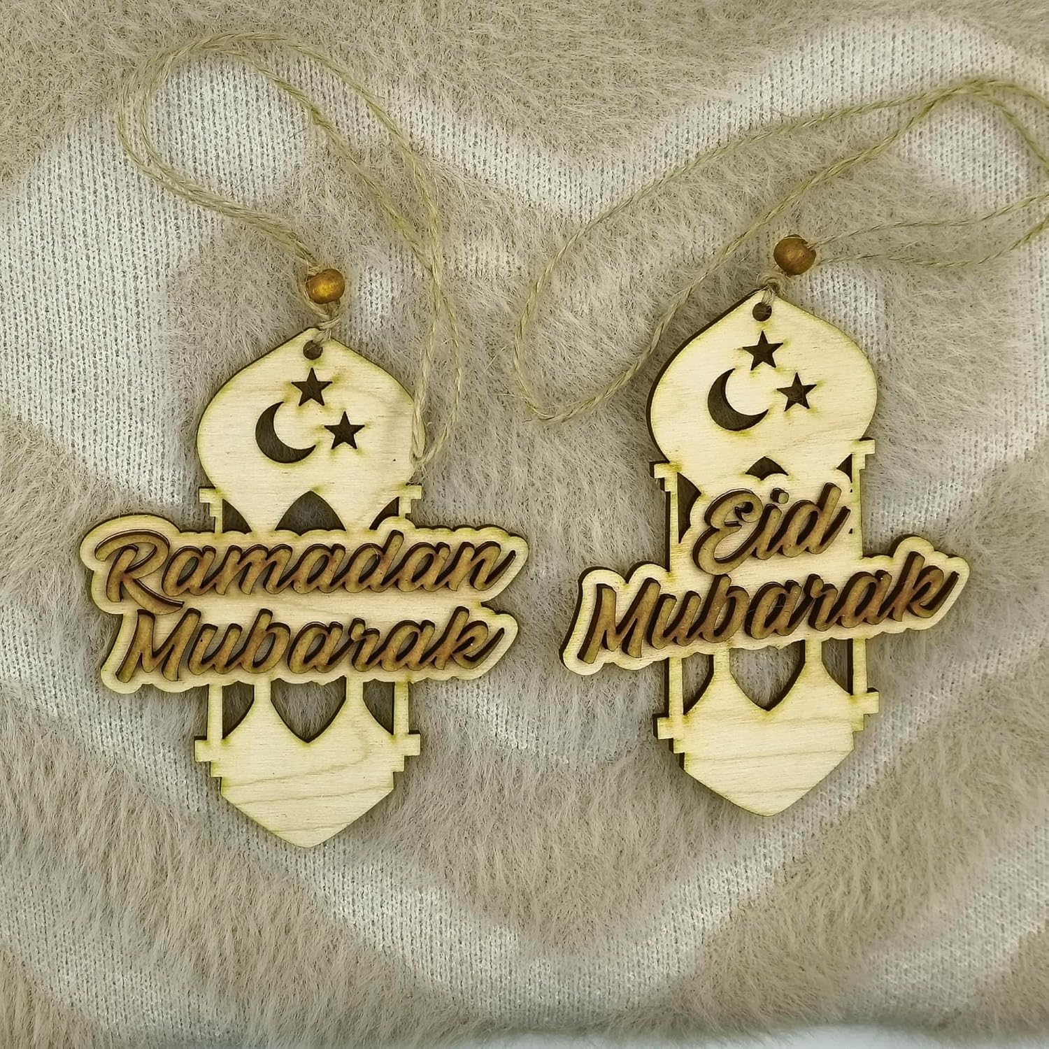 Two wooden ornaments with 'Ramadan Mubarak' and 'Eid Mubarak' text on a textured fabric background.