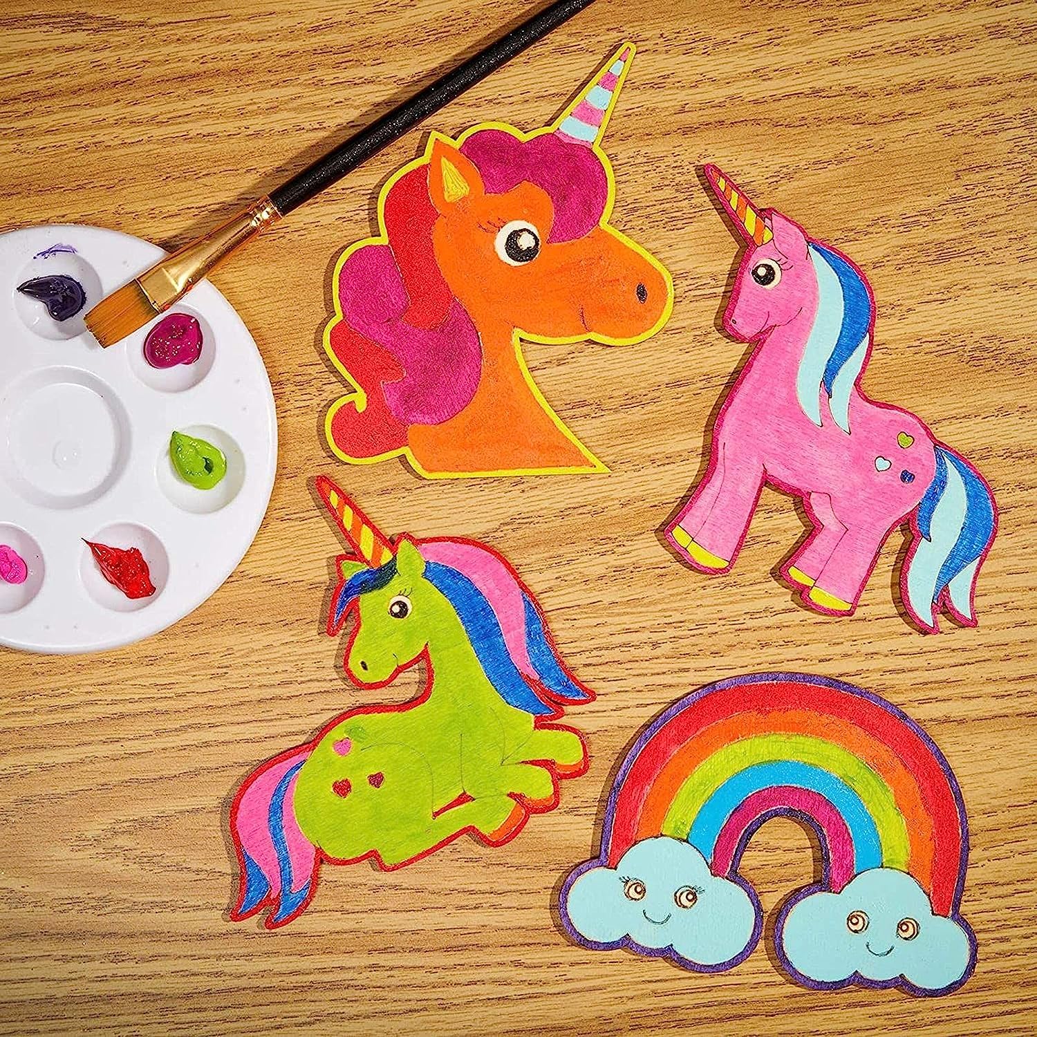 Colorful unicorn and rainbow craft items on a wooden surface with a paintbrush and palette.