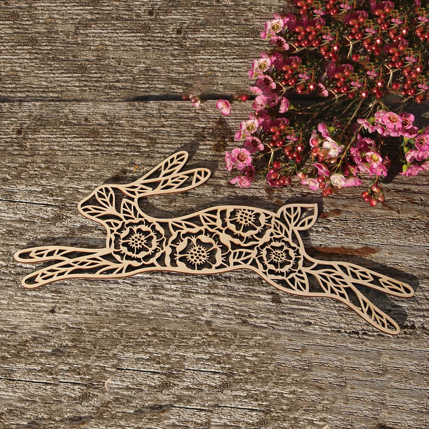 Decorative wooden hare with floral patterns on a wooden surface with pink flowers.