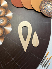 Wooden earring shapes on a dark surface with color swatches and tools.