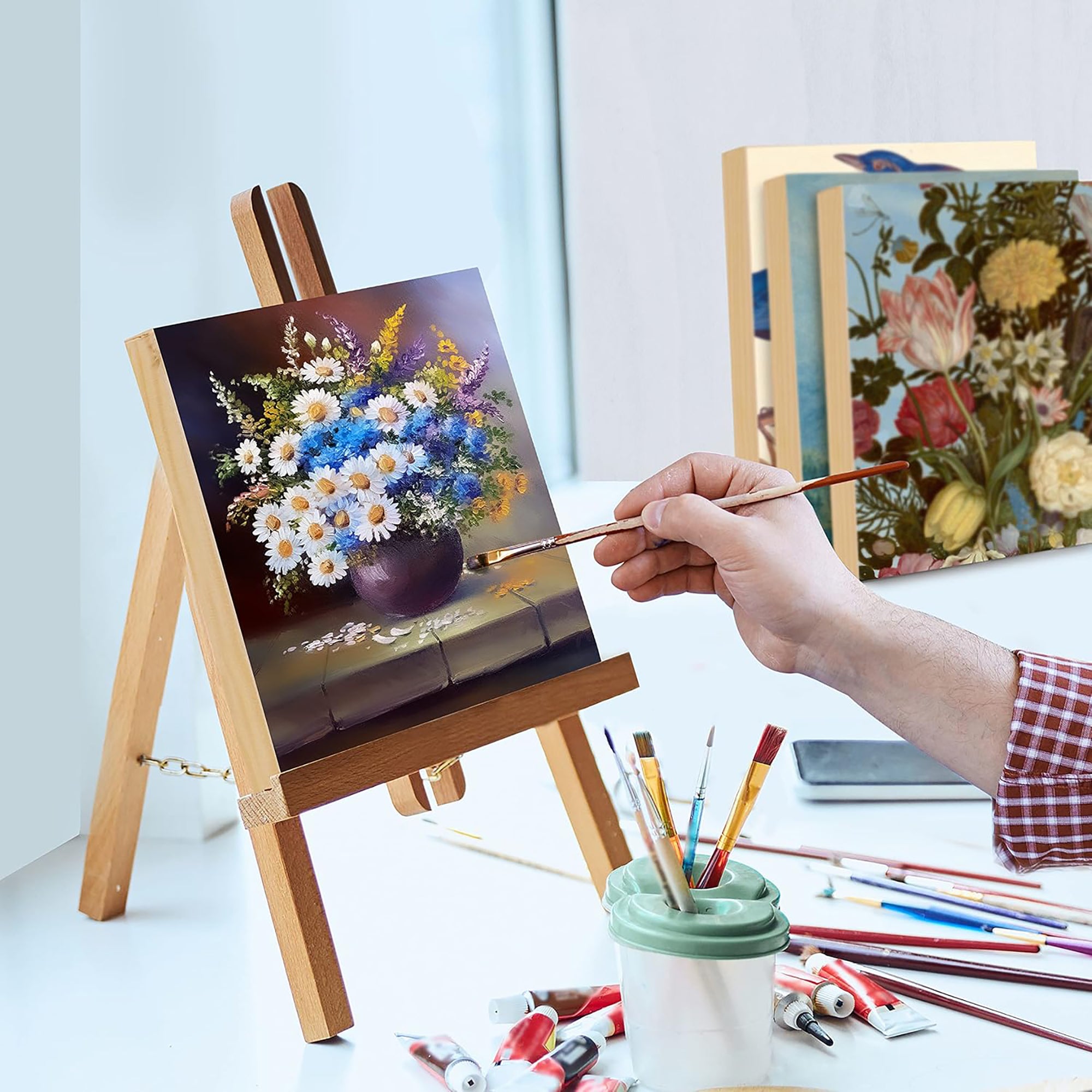 Person painting a floral scene on an easel with various art supplies around.