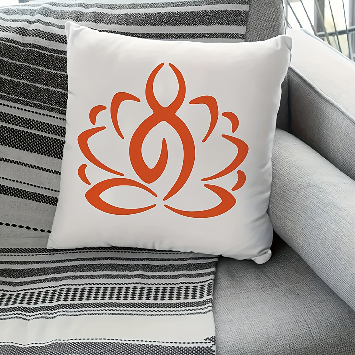 White pillow with orange symbol on a gray couch with striped blanket