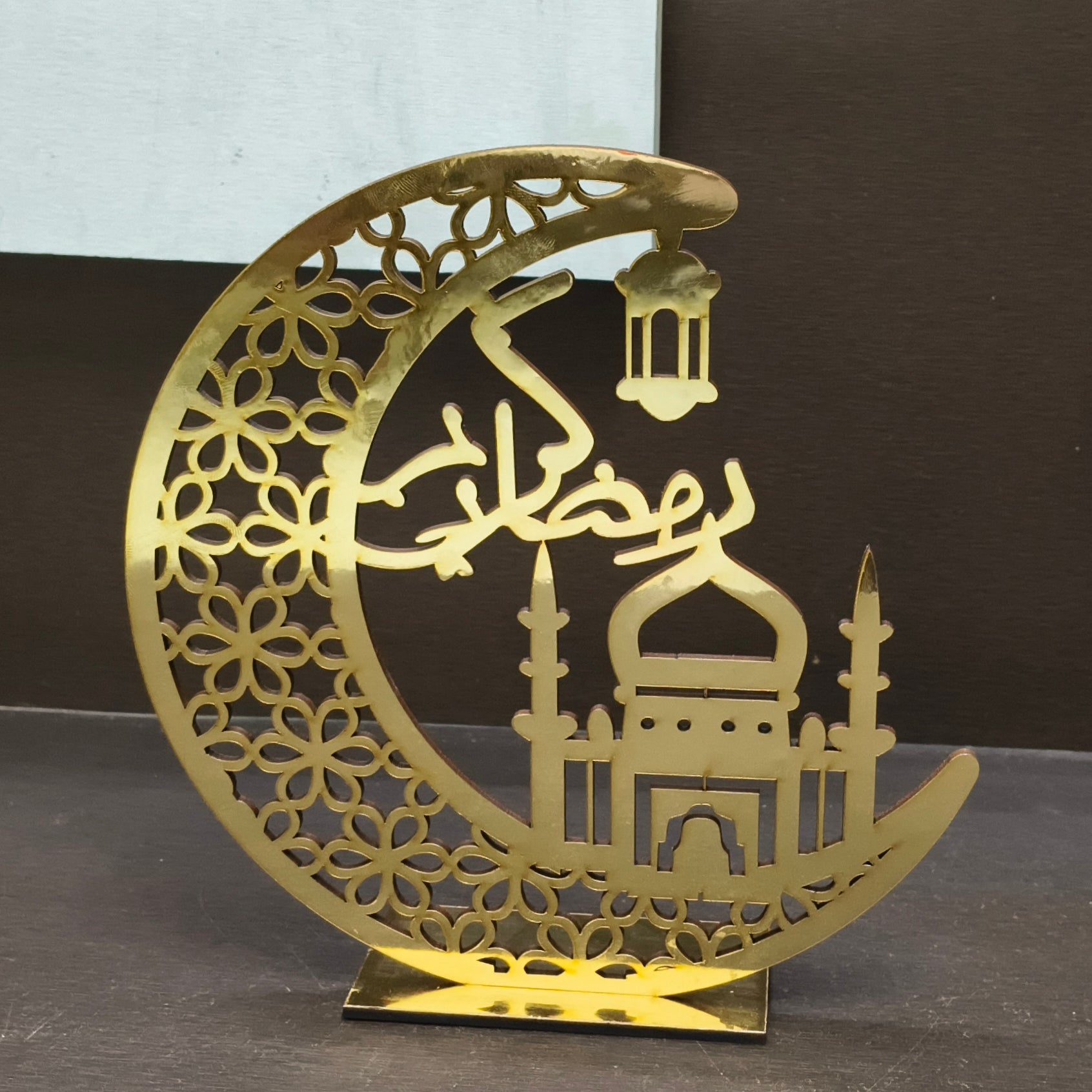 Decorative gold metal crescent moon with mosque silhouette and lantern on a dark background
