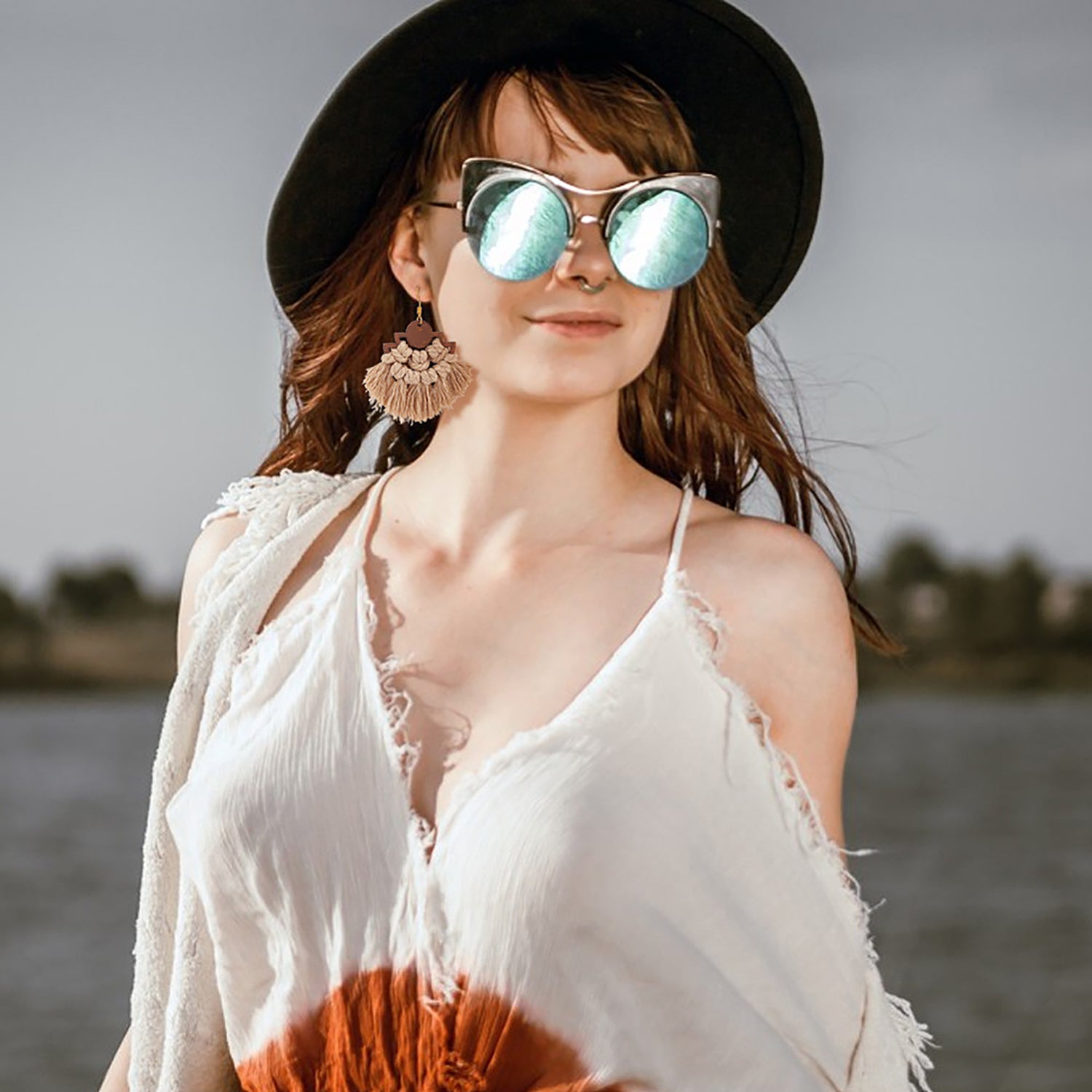 Woman wearing a black hat, white top, and sunglasses by a body of water.
