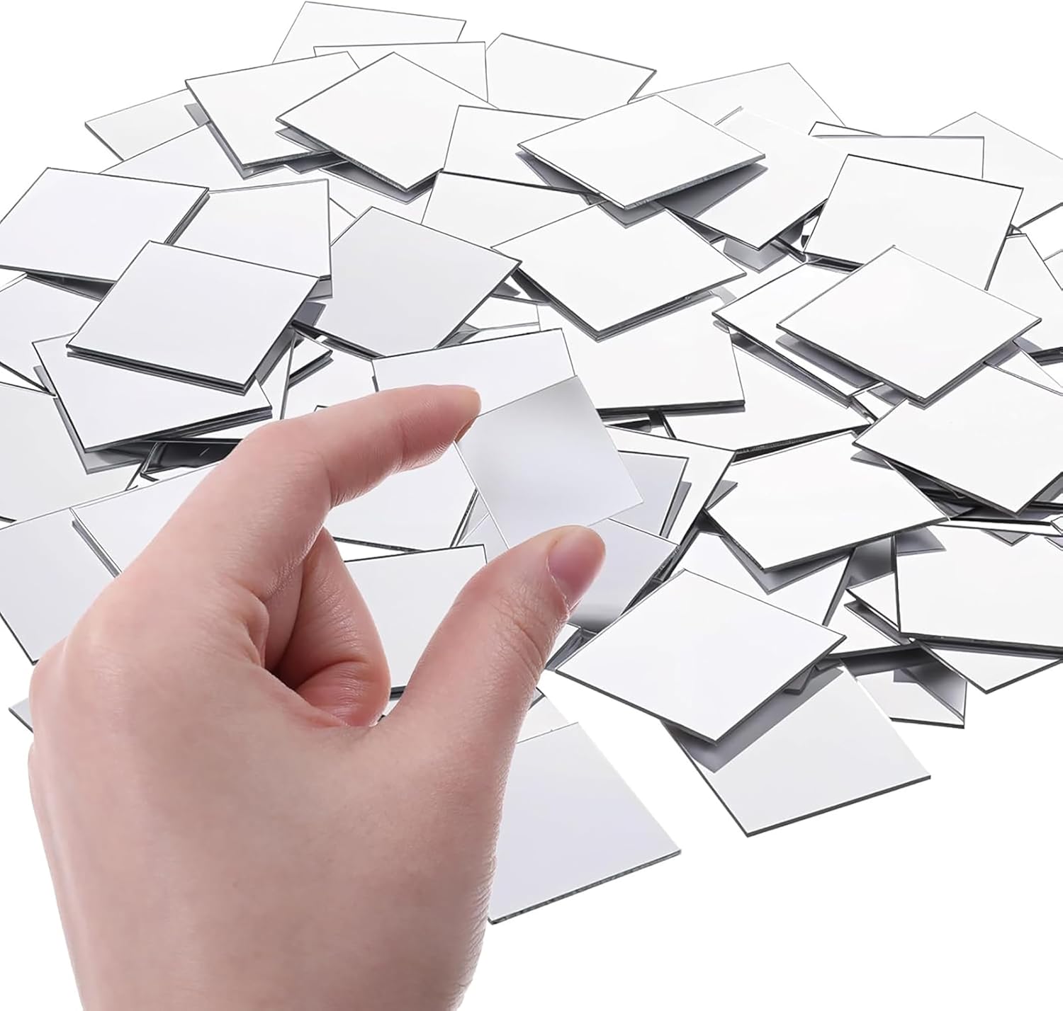 Hand holding a small square mirror over a pile of similar mirrors on a white background