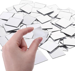 Hand holding a small square mirror over a pile of similar mirrors on a white background
