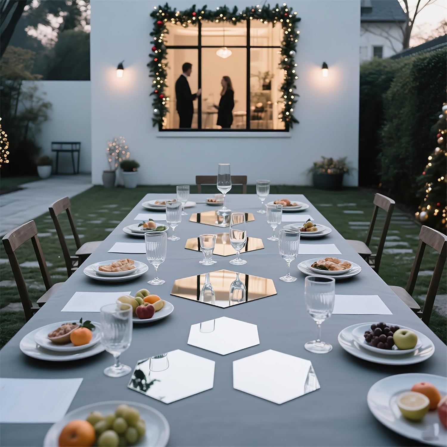 Dining table set outdoors with plates, glasses, and fruits, surrounded by chairs and decorative lights.