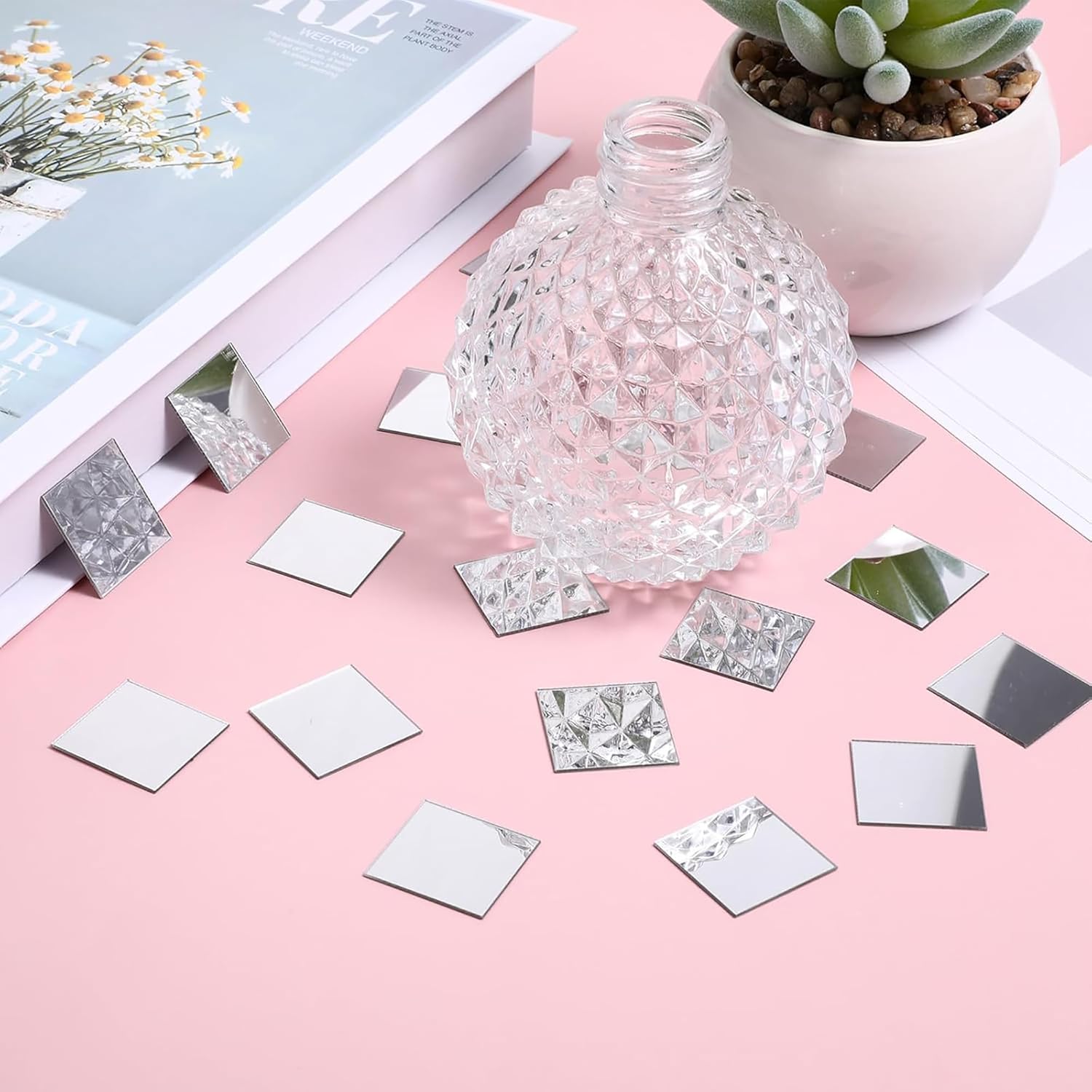 Clear glass vase with decorative mirror tiles on a pink surface
